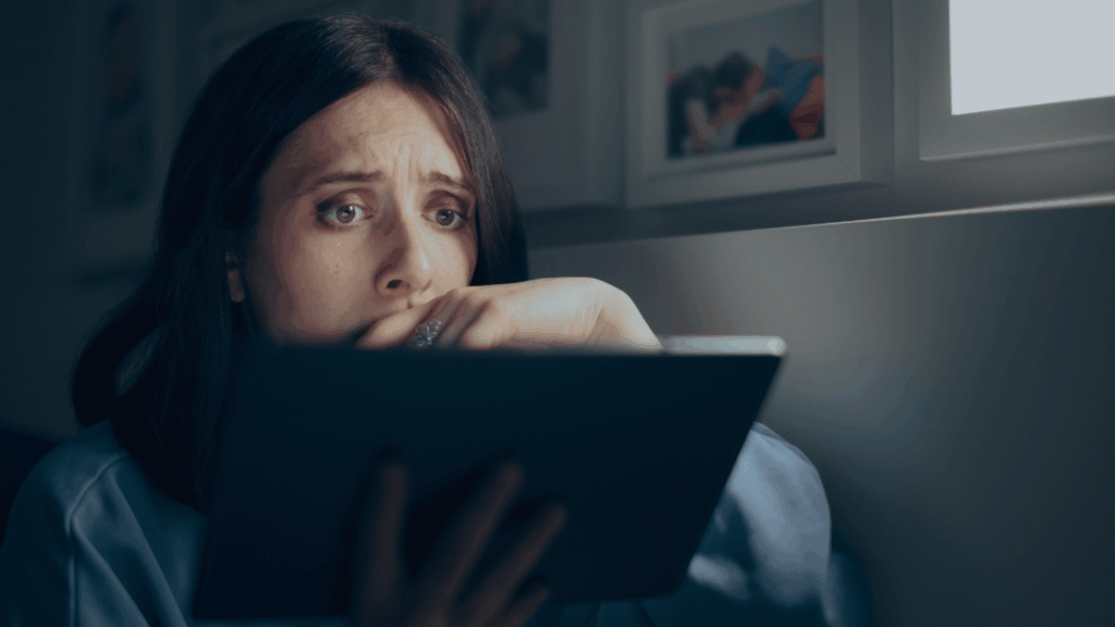 Frau sitzt im Dunkeln auf ihrem Sofa und schaut geschockt auf ihr Tablet